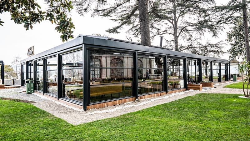 A garden restaurant enclosed with guillotine glass; black aluminium profiles and full-height glass panels.