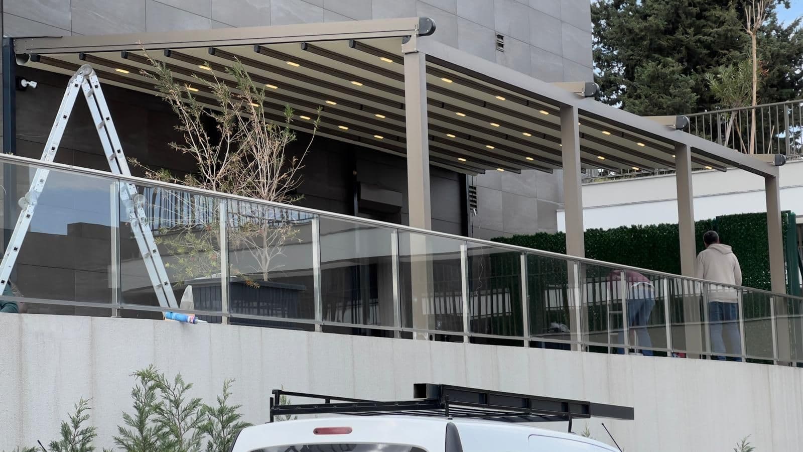 Ticari bir binanın terasına kurulmuş, LED aydınlatmalı geniş açıklıklı motorlu tente.